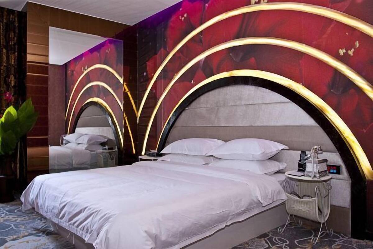Ein modernes Hotelzimmer mit einem großen Bett, einem Nachttisch mit Lampe und einer Wand mit floralem Wandbild.