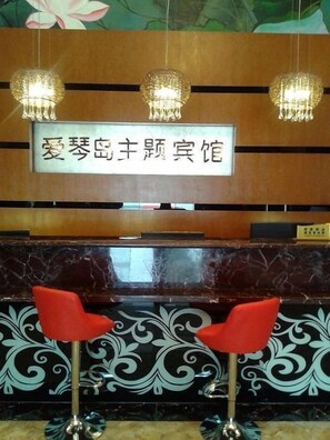 Un área de recepción con un cartel en caracteres chinos, una barra de mármol y dos sillas rojas.