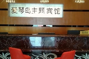 A reception desk with a sign, a marble counter, and two red chairs.