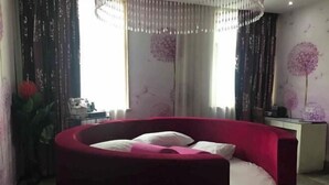 Ein Zimmer mit einem roten, runden Bett, einer Kandelaberleuchte, einem Schreibtisch und einer Wand mit Blumenwallpaper.
