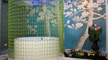 A bathroom with a large, round bathtub, a decorative tree mural, and a vase with flowers.