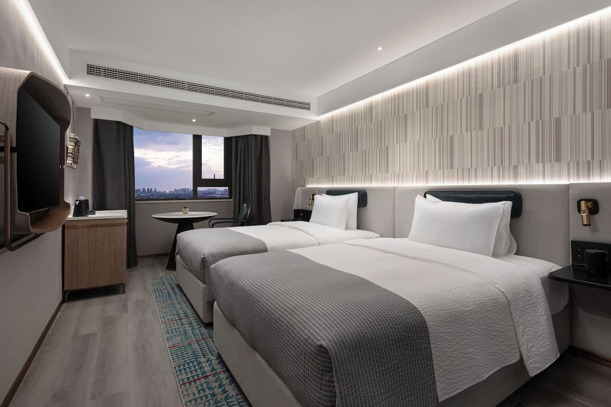 A modern hotel room with two beds, a small round table, a TV, and a city view.