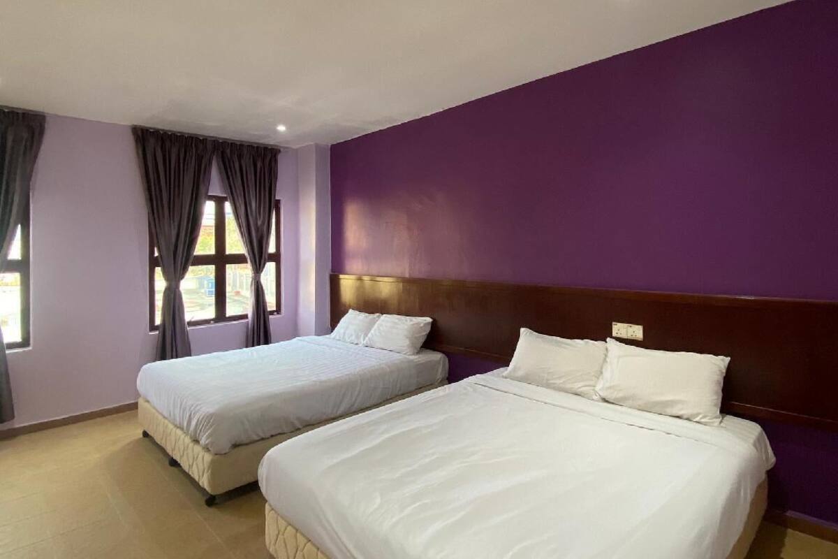 Habitación de hotel con dos camas, una pared morada y una ventana con cortinas.