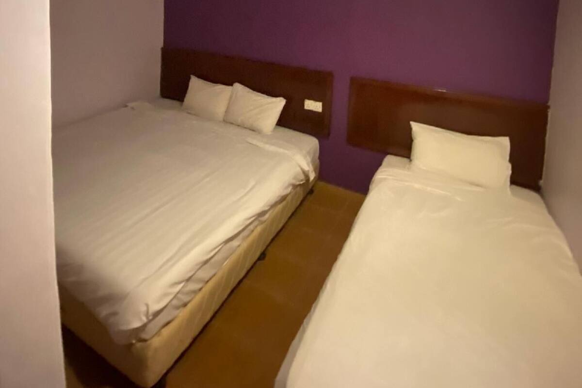 Habitación de hotel pequeña y con una cama doble, paredes moradas y una lámpara en el techo.