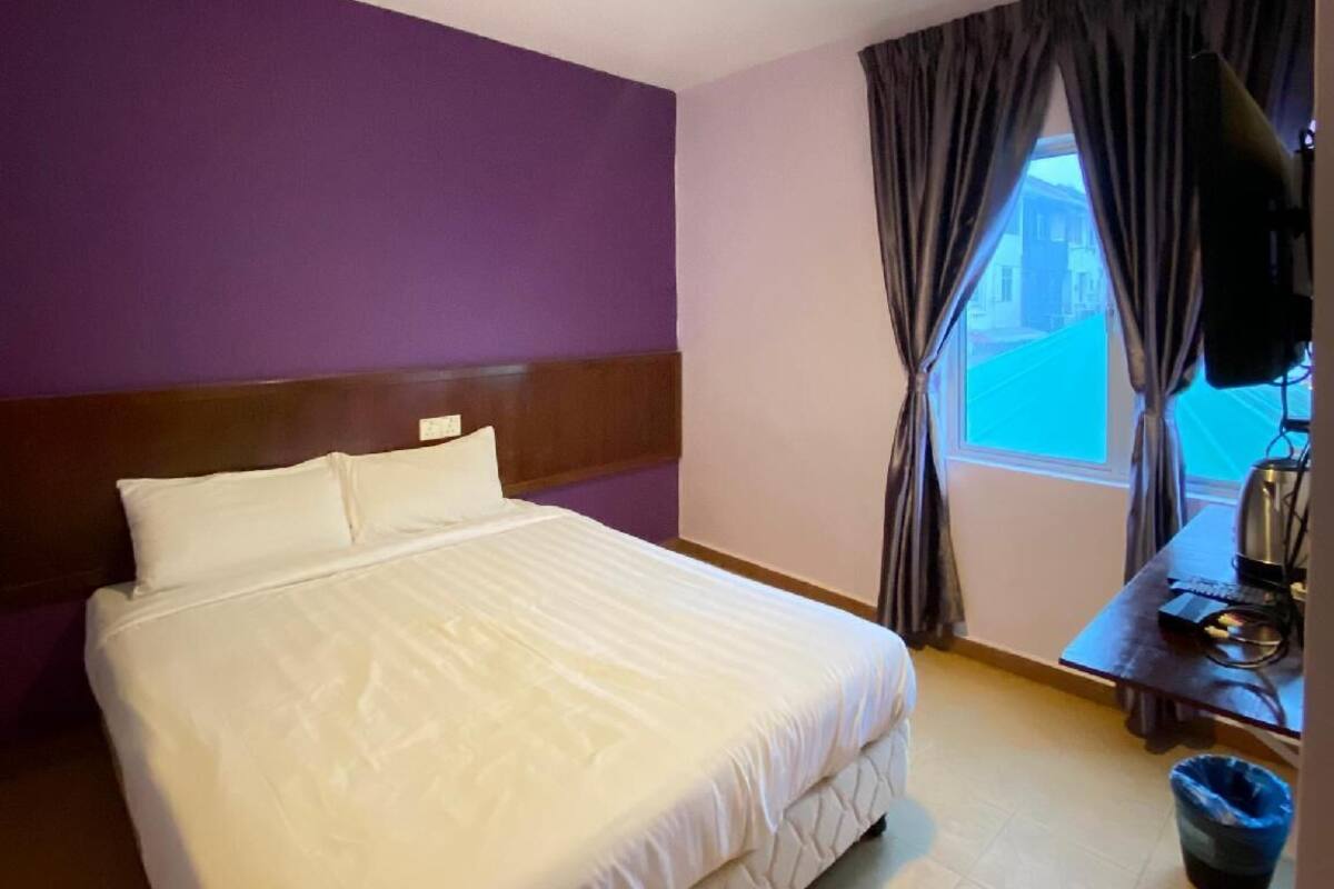 Una habitación de hotel con cama, escritorio con ordenador y ventana con cortinas.