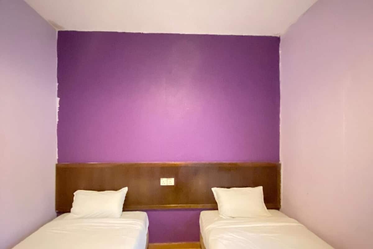 Una habitación con dos camas individuales, un cabecero de madera y una pared de acento morada.