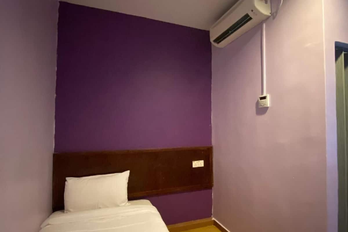 Una habitación de hotel con cama, paredes moradas, cabecero de madera, aire acondicionado y una puerta.