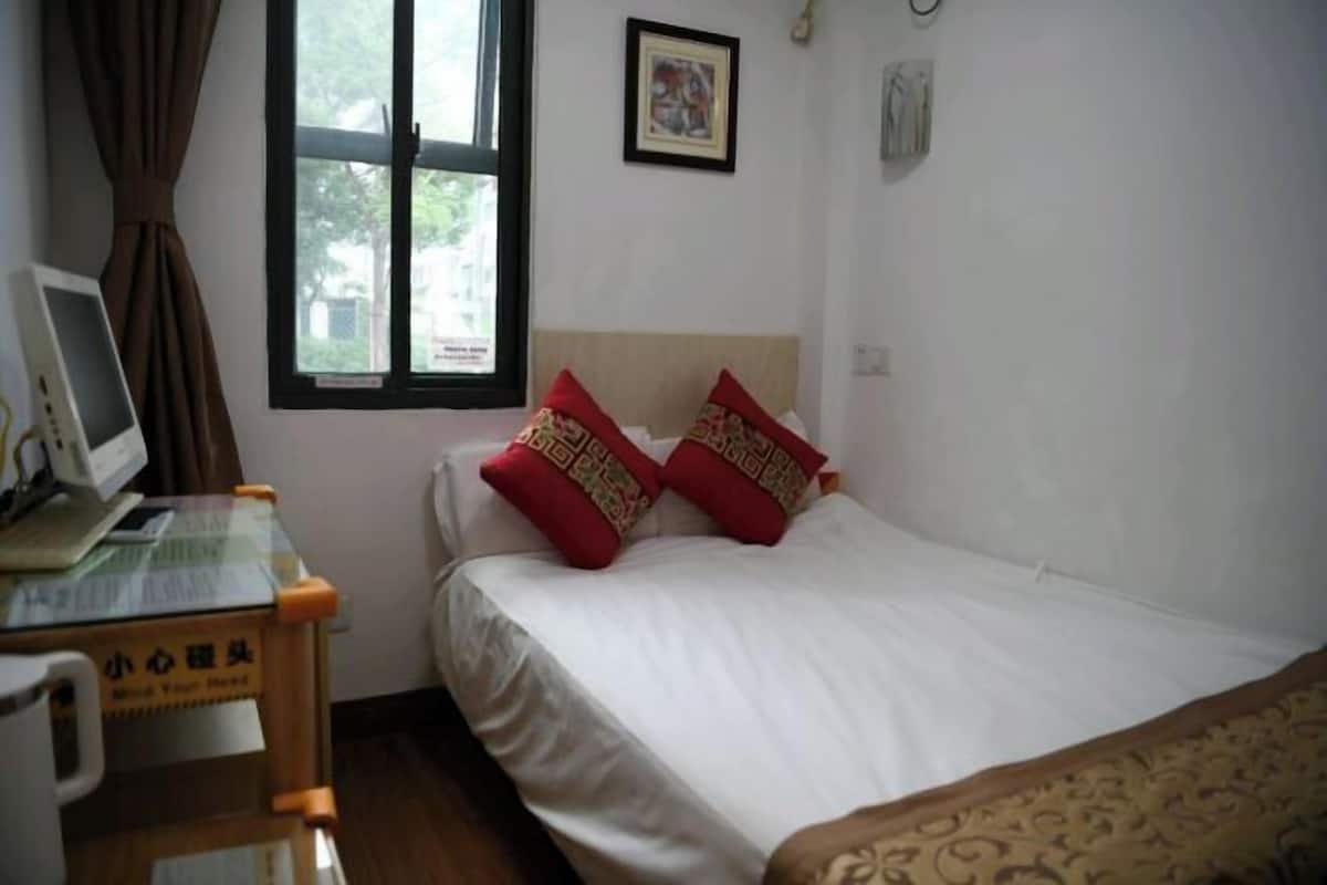 Une chambre à coucher avec un lit, un bureau avec un ordinateur et une fenêtre avec des rideaux.