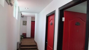 A hallway with a red door, a staircase, and potted plants.