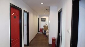 A narrow hallway with a red door on the left, a white door in the center, and a black door on the right. There are two red trash bins on the right side.