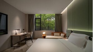 A modern hotel room with a large bed, a desk, and a chair. There is a window with curtains, a bedside table with a lamp, and a television mounted on the wall. - Wanda Yue Nantong (Nantong)
