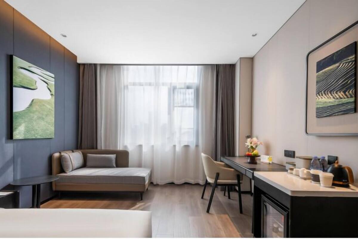 Moderni hotellihuone, jossa on vuodesohva, ruokailutila ja taideteoksia seinillä.