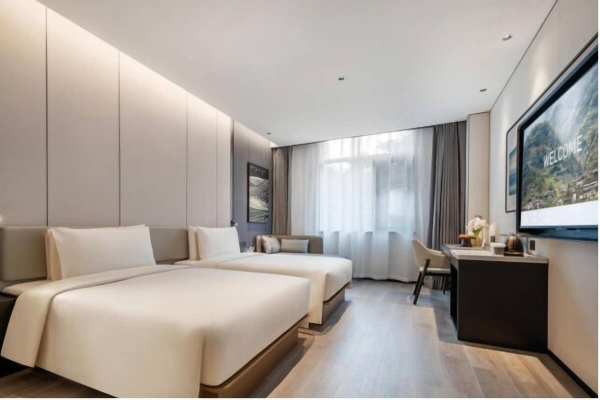 Moderni hotellihuone, jossa on kaksi sänkyä, työpöytä ja suuri ikkuna.