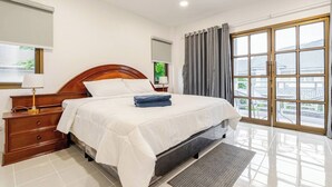 A hotel room with a large bed, a wooden dresser, a desk with a lamp, a large window with curtains, and a view of buildings outside. - New reno, 2 bed townhouse, best location, Patong (Pa Tong)