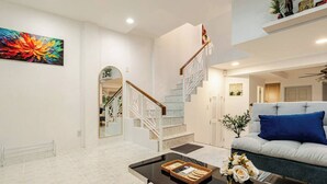 A spacious living room with a staircase, a sofa, a coffee table, and a colorful painting on the wall. - New reno, 2 bed townhouse, best location, Patong (Pa Tong)