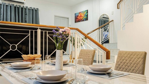 A dining area with a long table set for four, a vase with flowers, and a staircase in the background. - New reno, 2 bed townhouse, best location, Patong (Pa Tong)