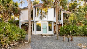 A two-story building with a light-colored exterior, a green door, and a gravel driveway. - Marsh View Treehouse Retreat on Fripp Island (Fripp Island)