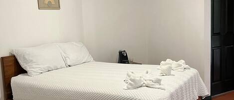 A neatly made bed with white linens and a quilted blanket, a bedside table with a phone and a glass, and a framed picture on the wall.