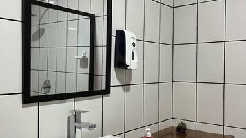 A bathroom with white tiled walls, a rectangular mirror with a black frame, a white sink with a wooden countertop, a soap dispenser, and a small glass container with a plant.