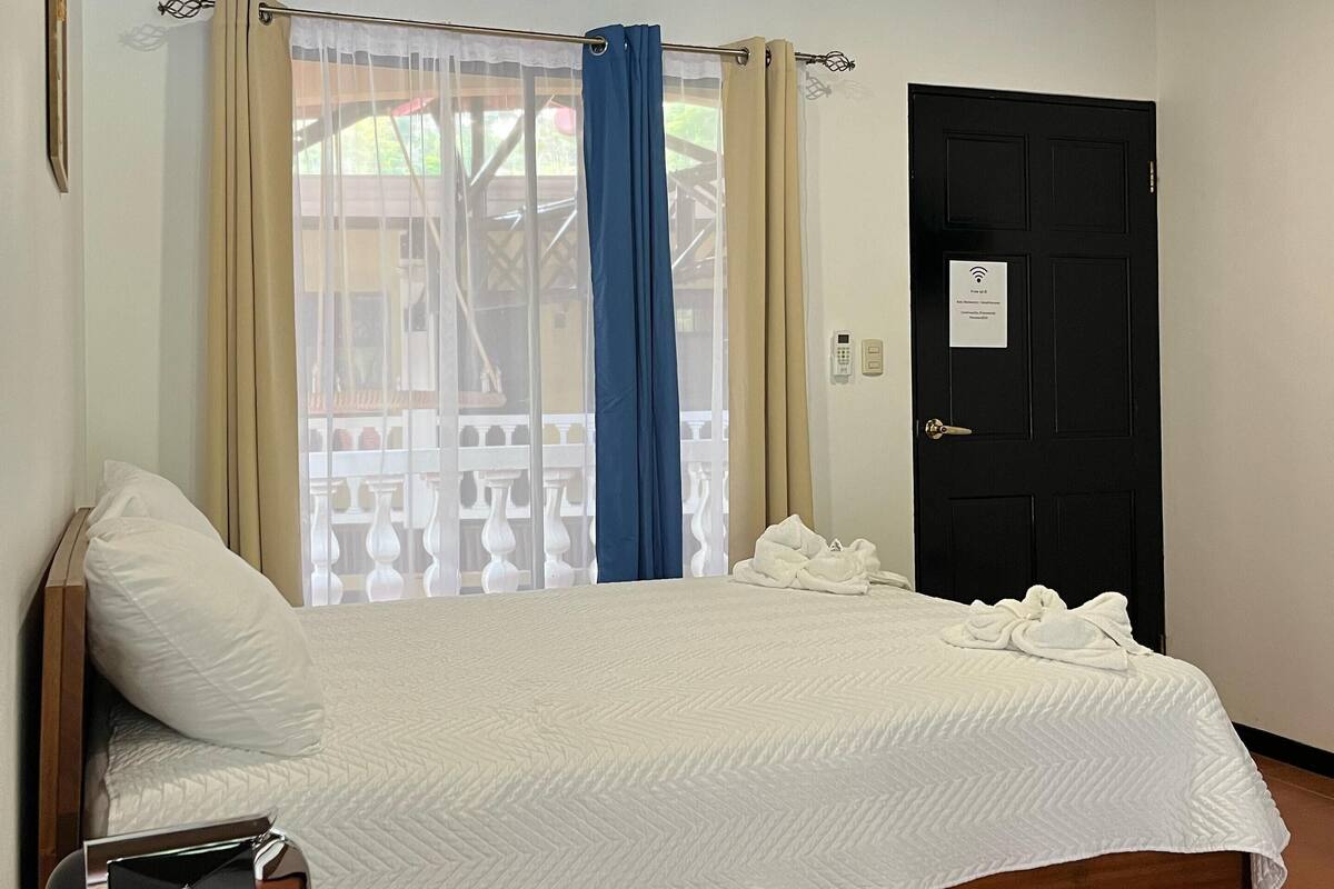A hotel room with a bed, a coffee maker, a door, and a window with curtains.