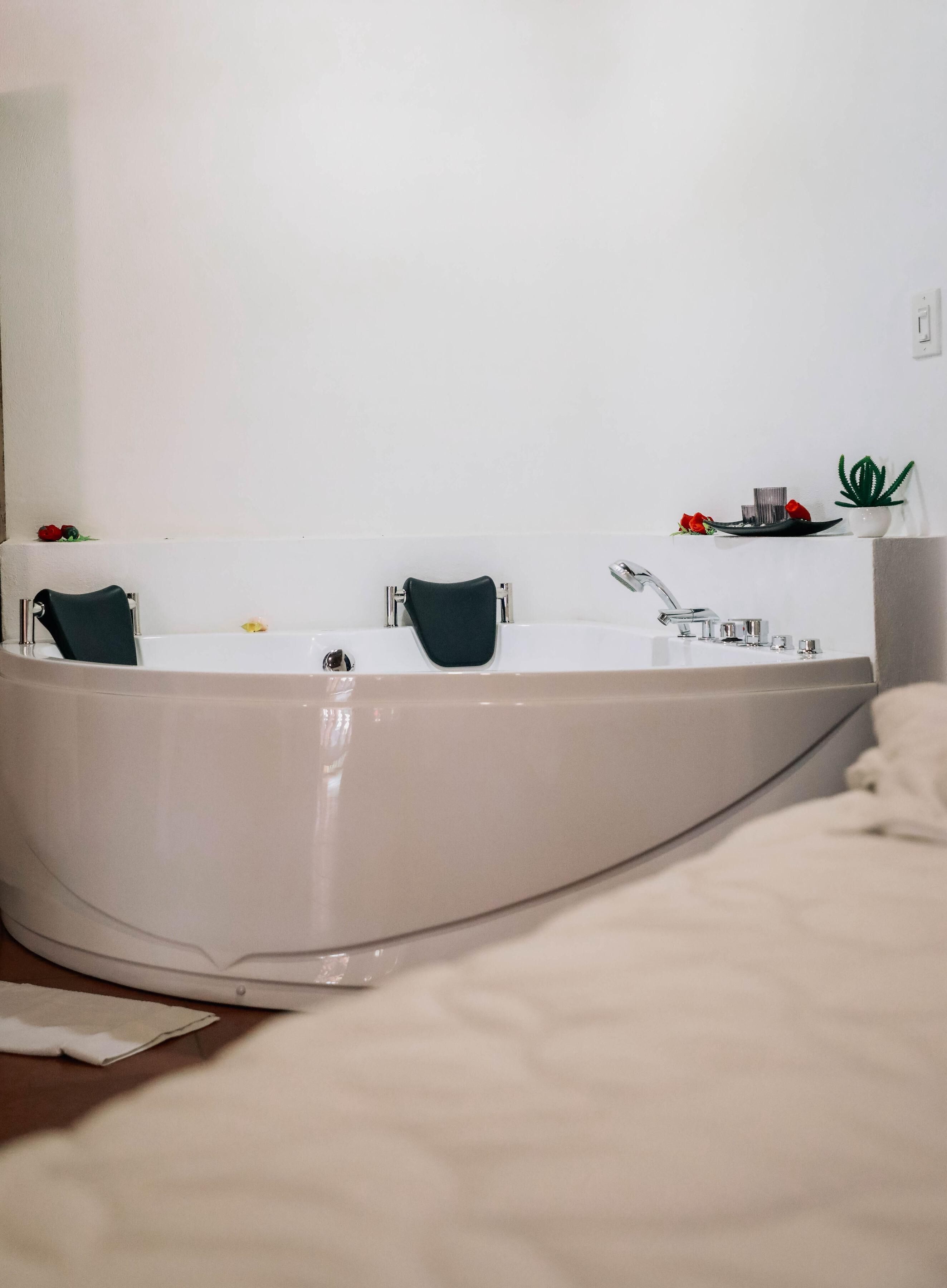 Un baño moderno con una bañera grande, un lavabo y un espejo. Hay elementos decorativos en la pared y una pequeña planta en el mostrador.