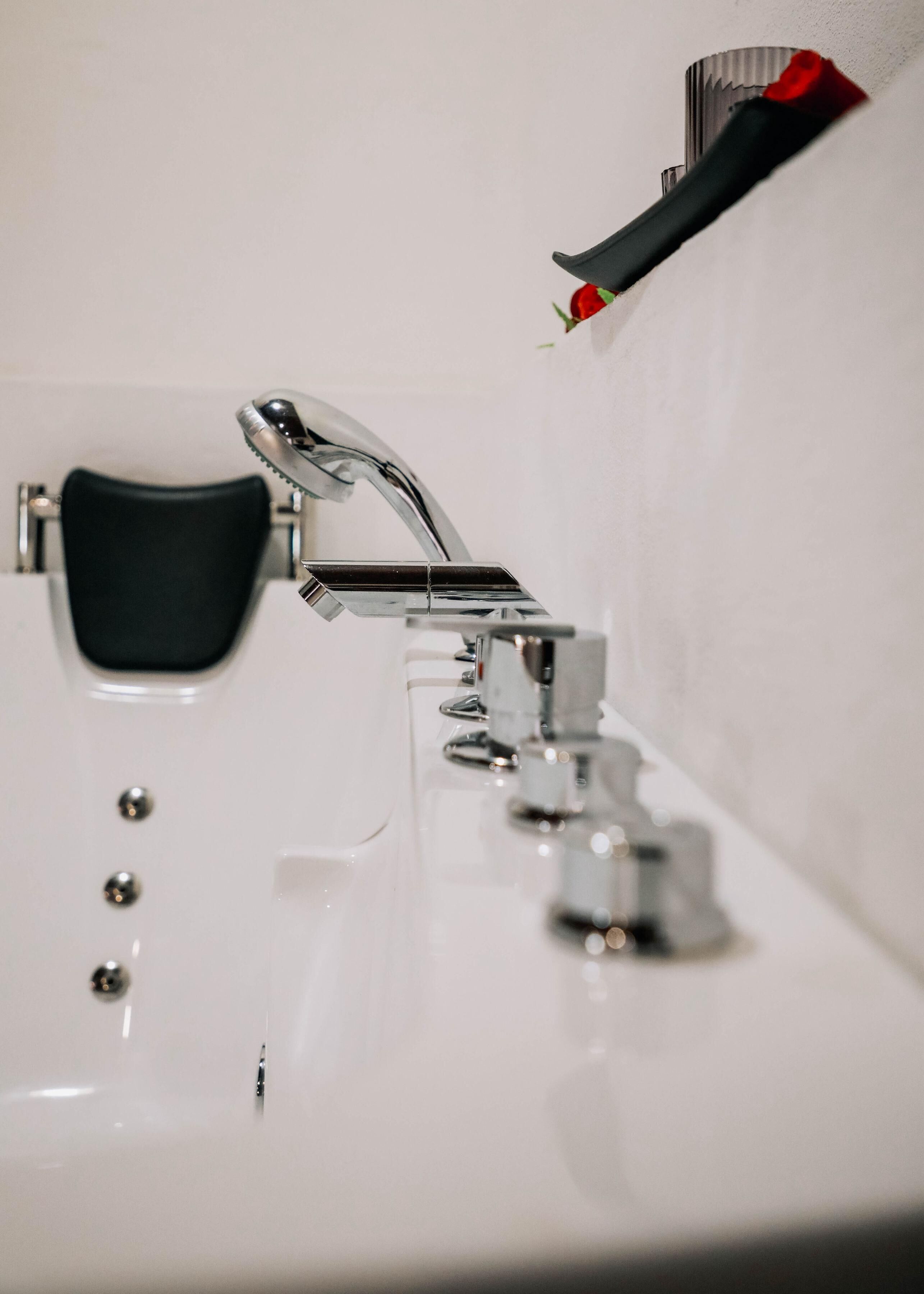 A bathroom with a chrome faucet, a black chair, and a red and black toothbrush holder on the wall.