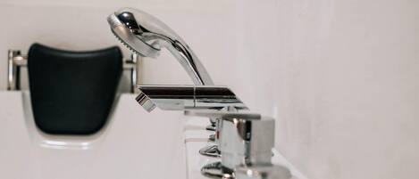 A bathroom with a chrome faucet, a black chair, and a red and black toothbrush holder on the wall.