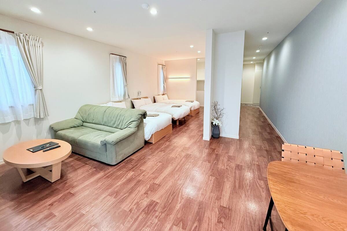Habitación de hotel con un sofá verde, dos camas, una mesita redonda y una silla de madera.