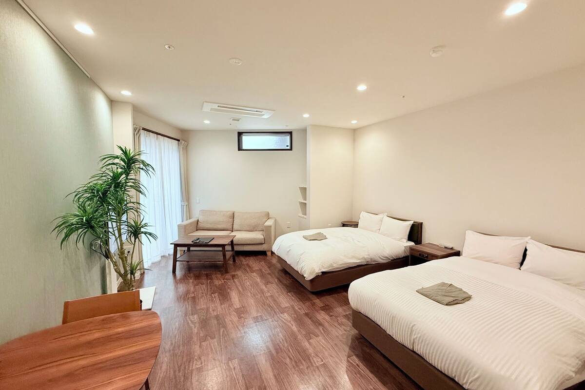 Habitación de hotel con suelo de madera, un sofá, una cama, una mesita pequeña y una planta en maceta.