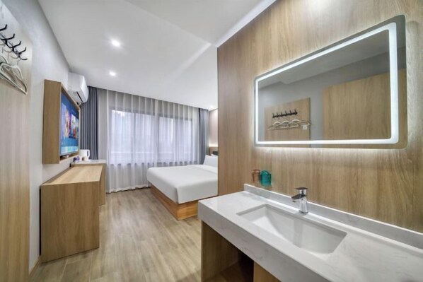 Una habitación de hotel moderna con suelo de madera, una cama grande, una mesita de noche, un lavamanos integrado y un espejo amplio.