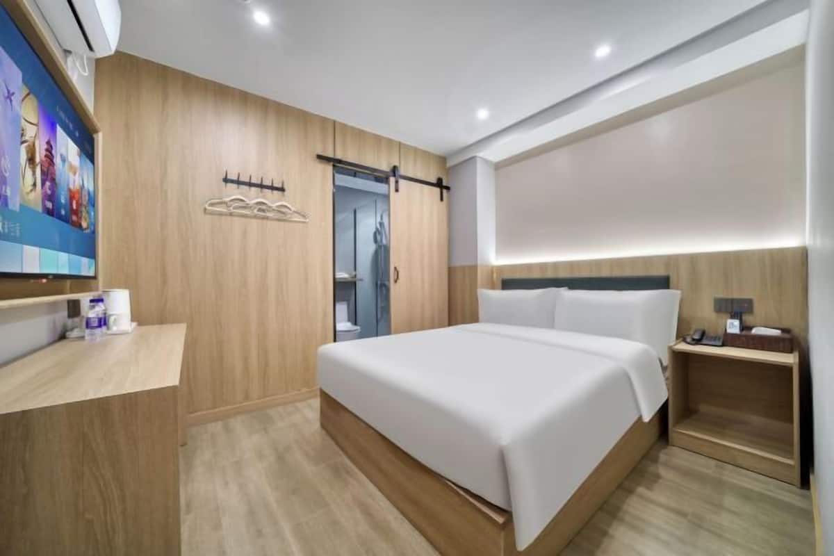 Une chambre d’hôtel moderne avec un mur lambrissé en bois, un grand lit, une table de chevet, une télévision et une armoire.