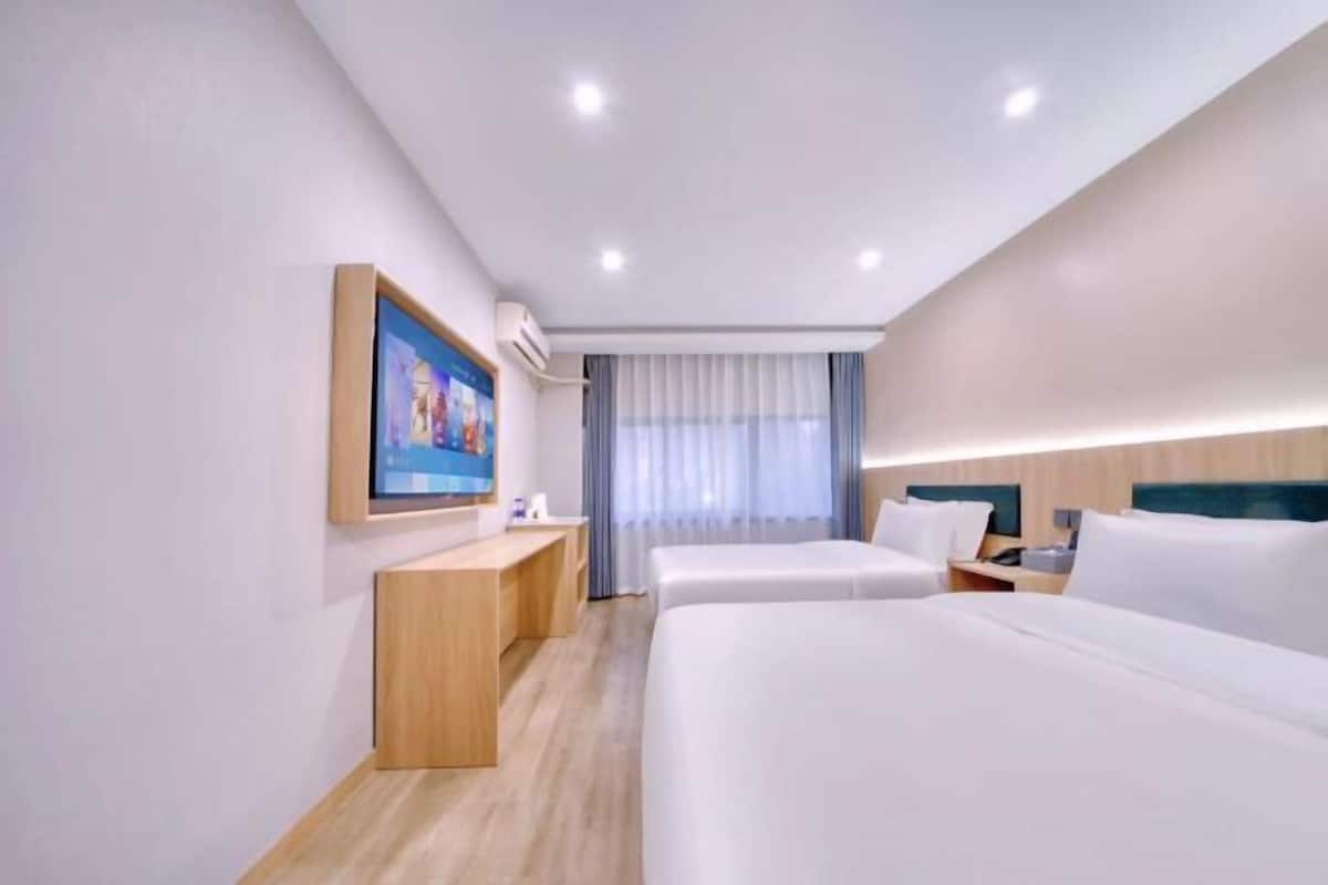 Une chambre d’hôtel avec deux lits, un bureau, un téléviseur fixé au mur et une fenêtre avec des rideaux.
