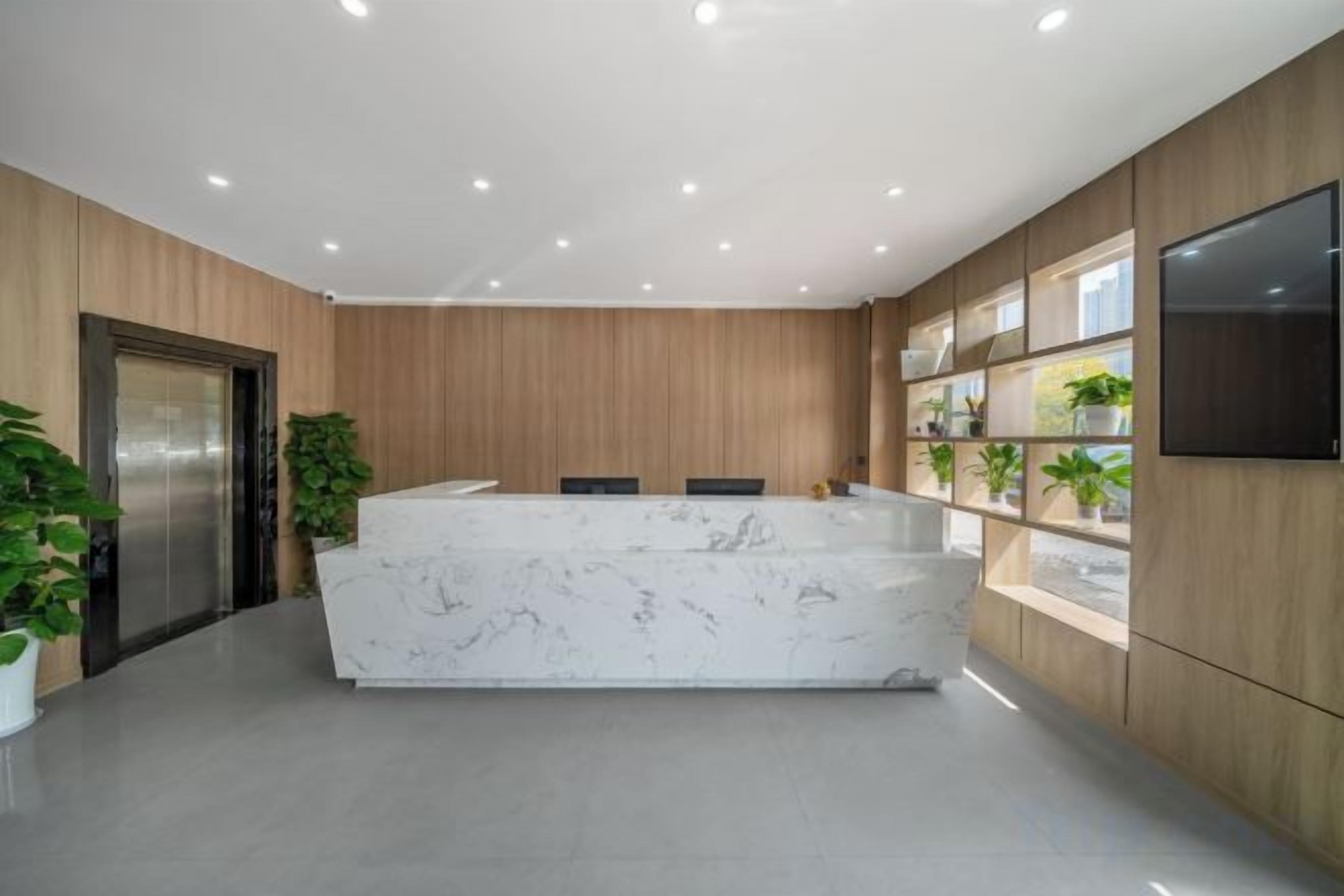 A reception area with a marble counter, wooden paneling, a flat-screen TV, and potted plants.