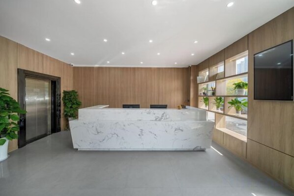 Una zona de recepción con mostrador de mármol, paneles de madera, televisor de pantalla plana y plantas en macetas.