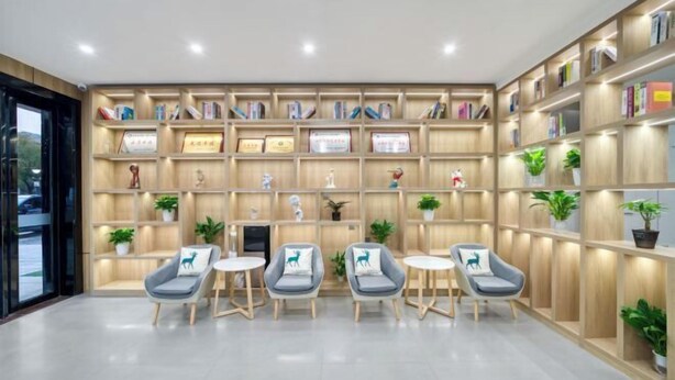 A modern library with wooden bookshelves, framed certificates, and decorative items. There are four grey armchairs with cushions and small round tables. - Hangzhou Melas Hotel (Hangzhou)