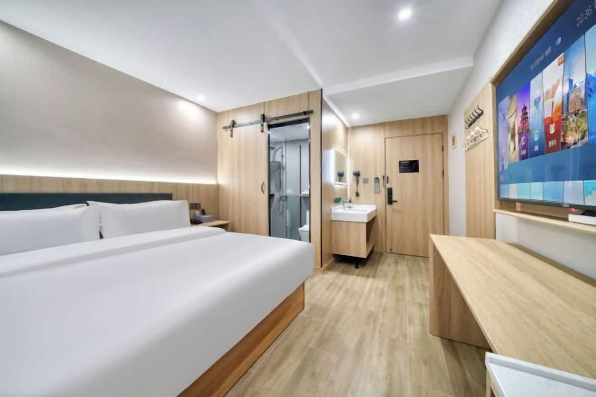 Une chambre d’hôtel moderne dotée d’un grand lit, d’un bureau, d’une salle de bain avec douche et d’un téléviseur fixé au mur.