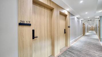 A hotel corridor with wooden doors, numbered room signs, and a carpeted floor.