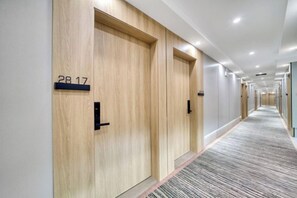A hotel corridor with wooden doors, numbered room signs, and a carpeted floor.