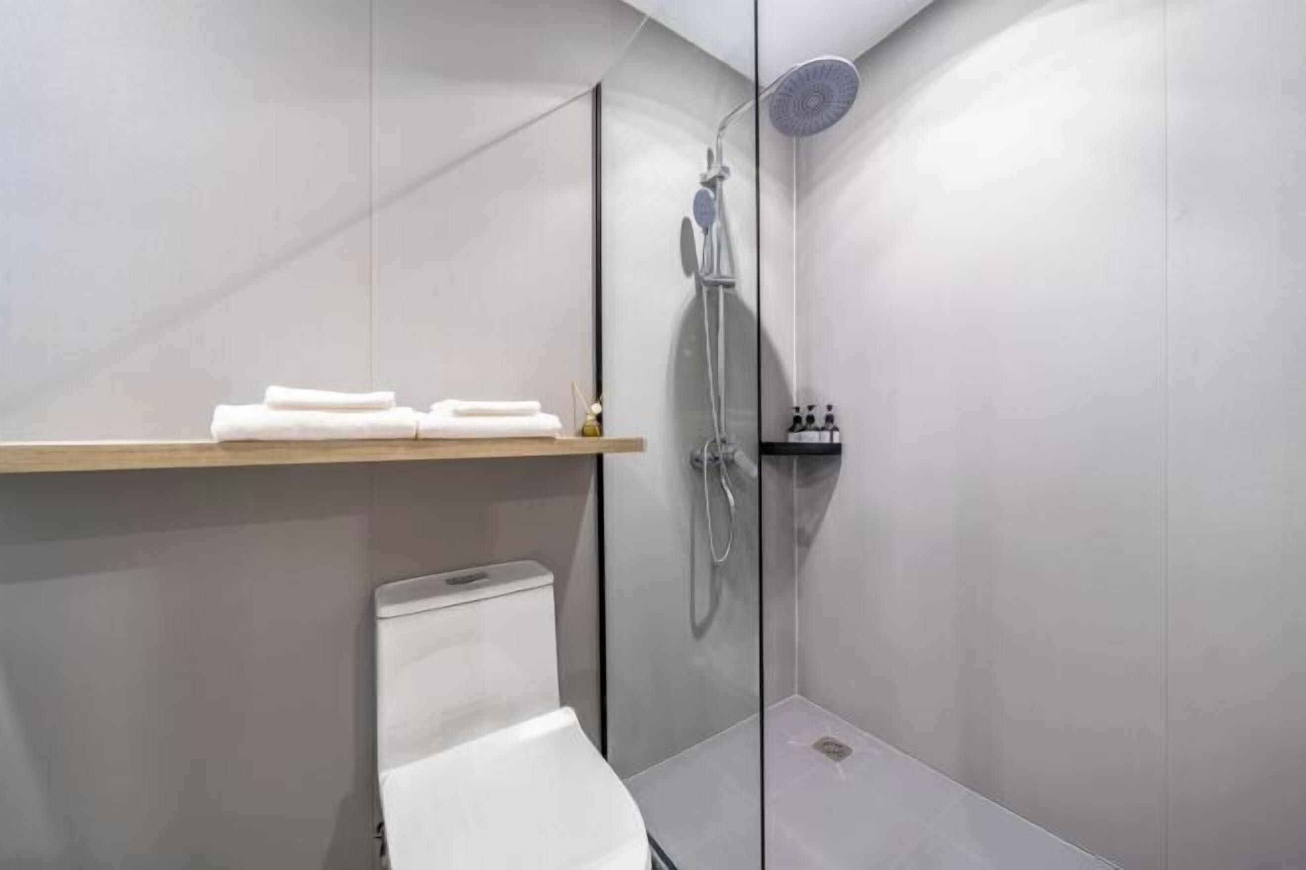 Ein modernes Badezimmer mit Duschkabine aus Glas, einer weißen Toilette und einem hölzernen Ablagebereich mit Handtüchern.