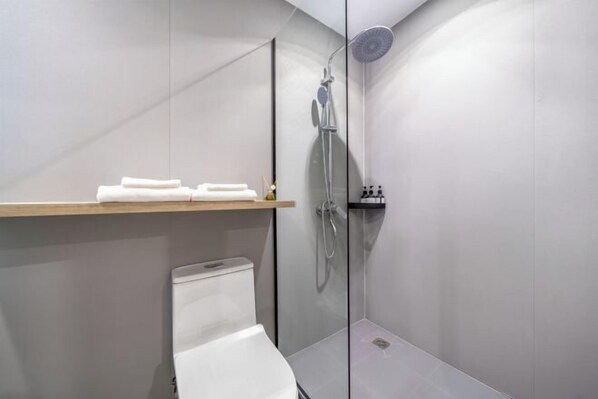 A modern bathroom with a glass shower enclosure, a white toilet, and a wooden shelf with towels.