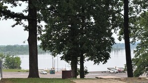 Un espace de stationnement avec des tables de pique-nique, un champ d’herbe et un lac en arrière-plan.