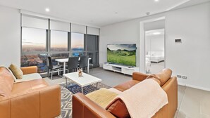 Ein modernes Wohnzimmer mit Ledersofas, einem Flachbildfernseher, einem Essbereich und großen Fenstern mit Blick auf die Stadt.