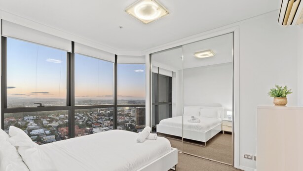 Ein modernes Hotelzimmer mit einem großen Bett, einer Sitzecke und Blick auf die Stadt durch raumhohe Fenster.