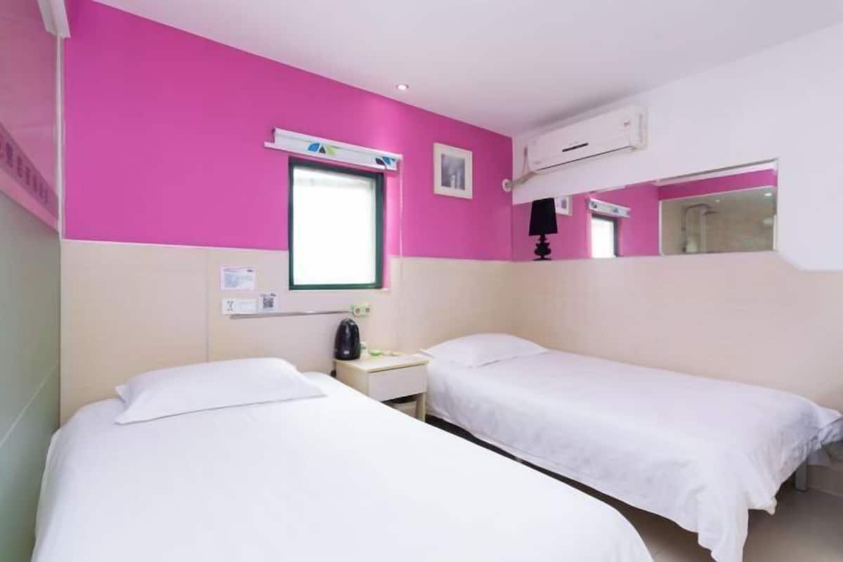 A room with two beds, a window, a bedside table, and a mirror.