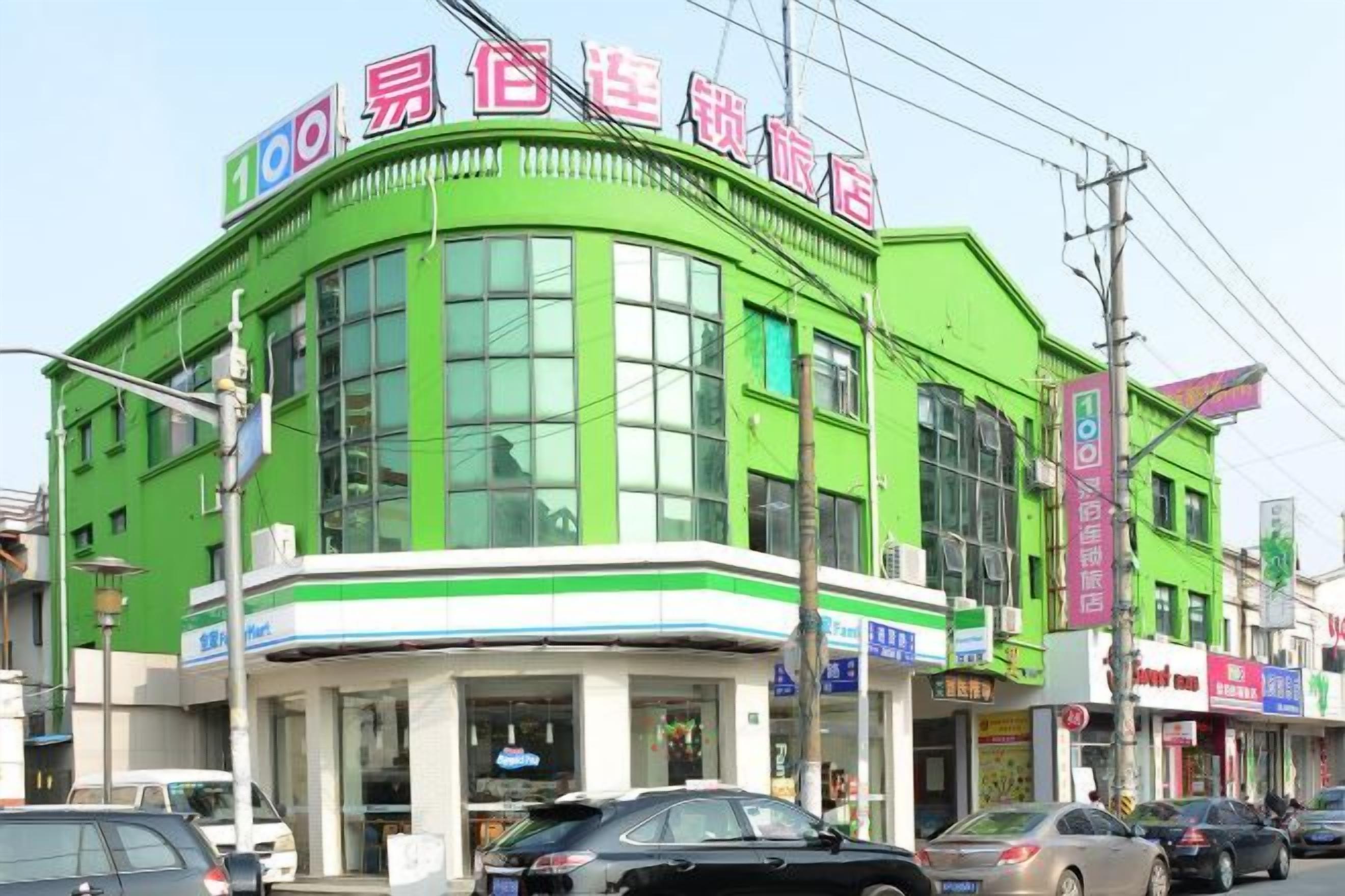 A green building with multiple storefronts on the ground floor, including a pharmacy and a convenience store.