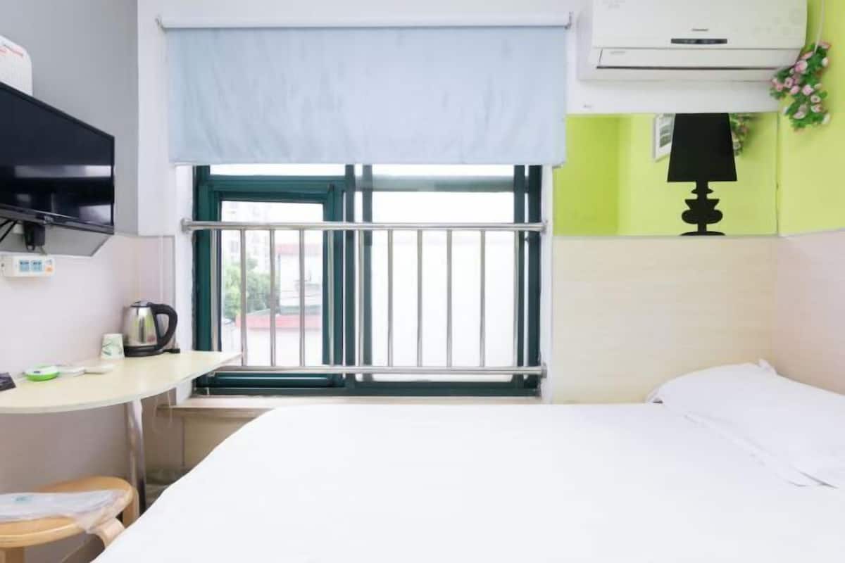 A room with a bed, a table with a kettle, a TV, a window with a view, and an air conditioner.
