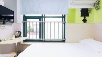 Quarto com cama, mesa com chaleira, televisão, janela com vista e ar condicionado.