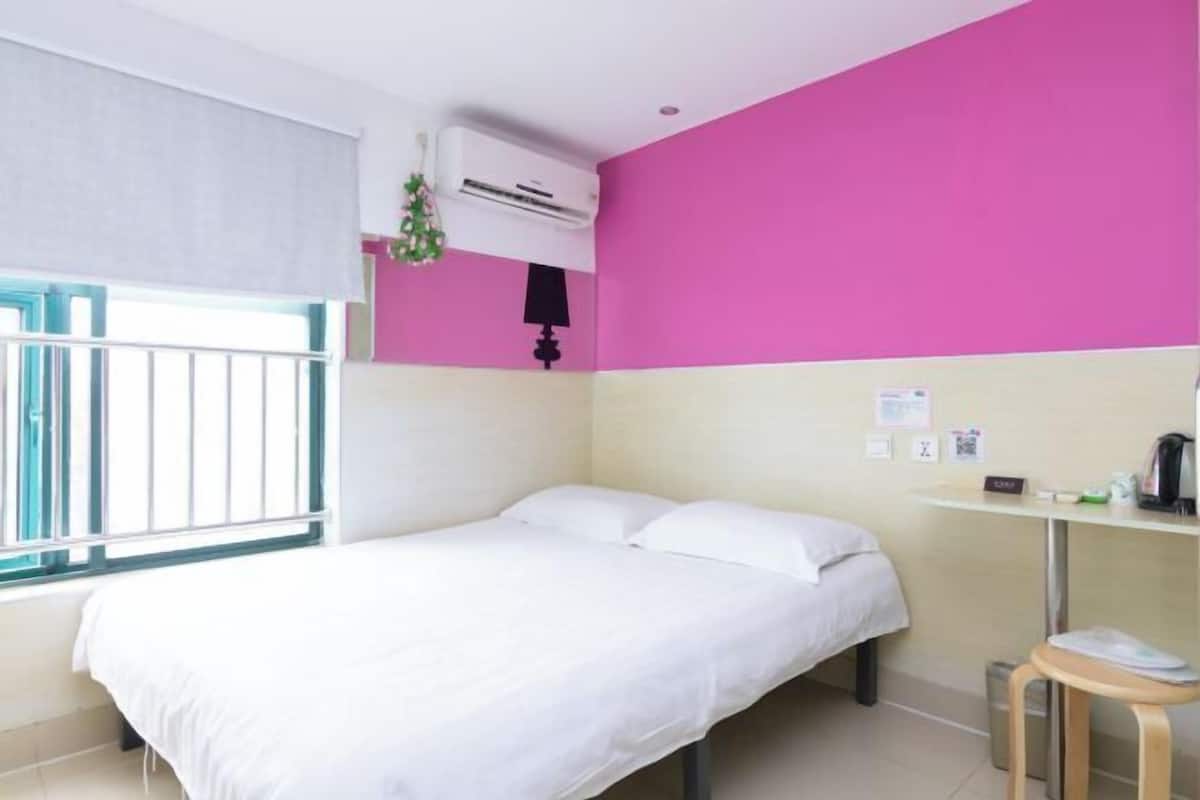 A room with a bed, a small table, an air conditioning unit, and a window with a view.