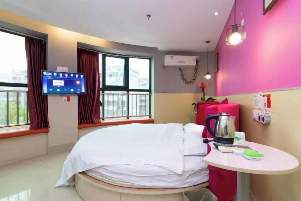 A hotel room with a bed, a small table with a kettle, a TV, and a window with curtains.