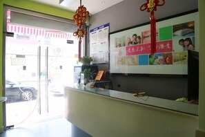 A reception desk with a glass partition, a bulletin board with photos and text, and a red decorative hanging. - 100 Inn (Shanghai Pudong Airport Chuansha) (Shanghai)